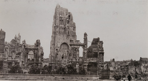 Civilians walking past the remains of a destroyed stone church with damaged buildings in the background