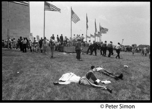Men lying on the grass near the Washington Monument, with protesters assembling in the background during the March on the Pentagon (mobilization on Washington)