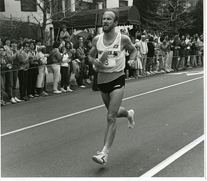 Runner, most likely in the Boston Marathon, carrying one of his shoes
