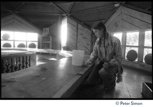 Young woman kneeling in a communal dining hall, cleaning tables, Lama Foundation