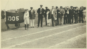Members of the class of 1905 standing outside in a line behind a 1905 banner on a track