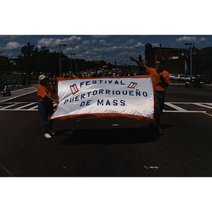 Two men carry a banner reading, "Festival Puertorriqueño de Mass."
