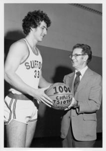 Suffolk University men's basketball player Chris Tsiotos (#33) accepts ceremonial basketball recognizing his 1,000 career points from Coach Charles Law, 1975