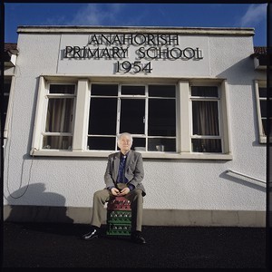 Seamus Heaney at his old primary school, Anahorish, Bellaghy, Co. Derry, sitting on a milk crate and standing in front of school