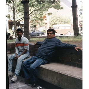 Two men sitting on a ledge in the park.