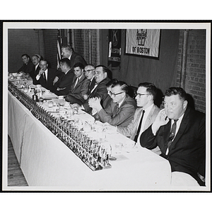 William J. Lynch, fourth from left, seated at a long table with many small trophies alongside twelve other men at a Charlestown Kiwanis Club event