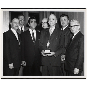 A man, holding a trophy, poses with six other men, including William J. Lynch, on the far left