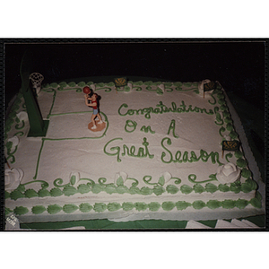 A shot of a cake addorned with a figurene and hoop commemorating a basketball season