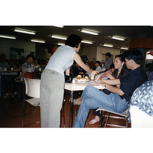 Woman holds a microphone while a guest speaks at a Chinese Resident Association meeting