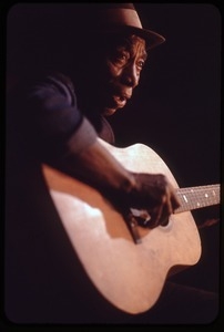 Mississippi John Hurt: studio portrait, seated, playing guitar