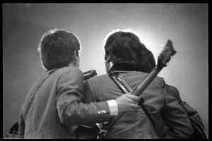 Rear view of (l. to r.) Paul McCartney, John Lennon, and George Harrison (obscured) huddled around a microphone in concert with the Beatles, Washington Coliseum