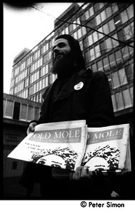 Bearded man selling the Old Mole outside the Cambridge Trust Co.
