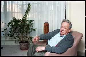 Fine art photographer Aaron Siskind: portrait with a potted plant in the background, while seated in a armchair in his living room