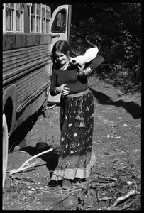 Commune woman in a peasant dress, with a Siamese cat on her shoulder, standing next to a bus, Earth People's Park