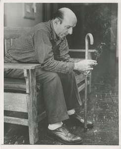 A man with a cane sits smoking on a bench