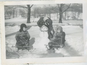 Paul and Joel Kahn on sleds with their mother Bernice and a snowman