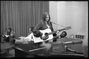 Judy Collins playing guitar by a piano (Michael Sahl in background, center)