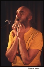 Ram Dass with his hands on his beard, on stage with Amazing Grace