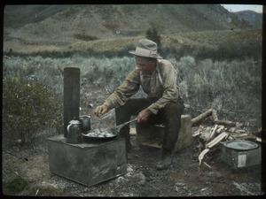 Man cooking on camp stove in dry, hilly country