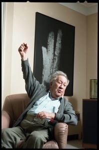 Fine art photographer Aaron Siskind: raising his fist while seated in a armchair in his living room