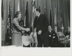 A woman holds the 1966 President's Trophy and shakes Hubert Humphrey's hand