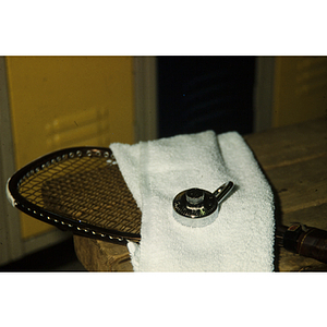 Racket, towel and combination lock stacked on a locker room bench