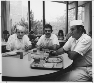 Robert Sacco seated, center, with two bakers in cafeteria