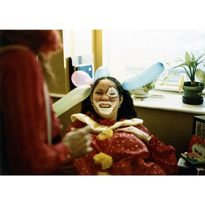 Woman dressed as a clown, seated in chair, smiling and laughing with a male clown, before their performance in the Three Kings' Day celebration at La Alianza Hispana, Roxbury, Mass