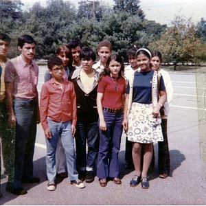 Six male youths, four female youths, and one adult woman pose for a group photograph in the parking lot adjacent to a park