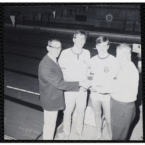 Two swimmers holding up their trophy while their coach shakes hands with the presenter at the Boys' Clubs of America New England Regional Swimming Championships at Harvard