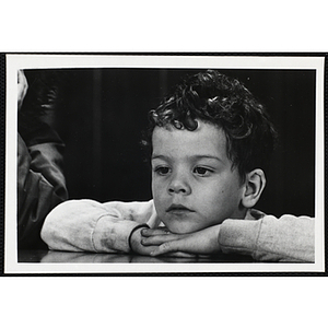 A young boy from the Boys' Clubs of Boston resting his head in his arms on the table