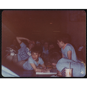 Several boys and girls in blue t-shirts gather around a table at the Charlestown Boys' Club Art Exhibit