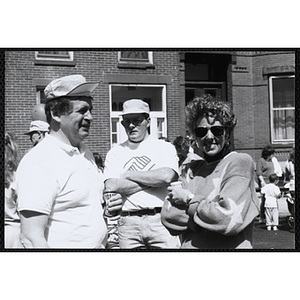 A man, facing right, stands with a woman wearing sunglasses while another man stands behind them with his arms crossed at the Boys and Girls Clubs of Boston 100th Anniversary Celebration Street Fair