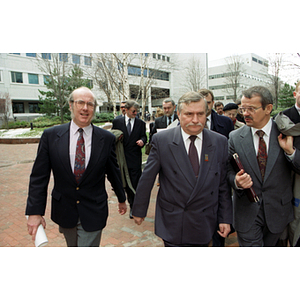 Dean Lowndes, Lech Walesa, and another man walk through the Snell Library quadrangle