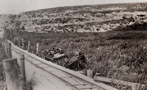 View of overturned carts alongside a narrow gauge railway running across a field
