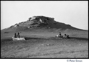 Children sitting on the dirt in an arid New Mexico landscape, rock outcrop in the background