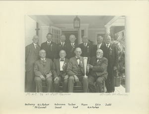 Eleven men from the class of 1876 sitting on a porch and holding a trophy