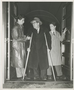 Two young men assisting a man on crutches as he exits a building