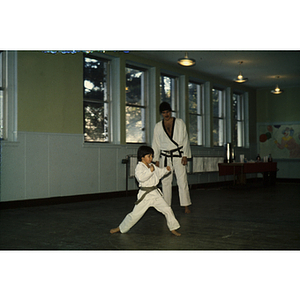 Boy practicing martial arts as an instructor looks on