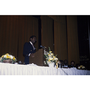 Man speaking at a lectern adorned with flowers