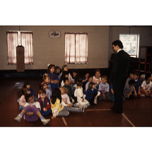 Man speaking to children seated on the floor of a gymnasium at the Eastern Middlesex Family YMCA