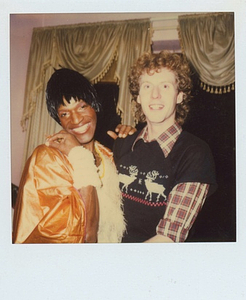 A Photograph of Marsha P. Johnson Wearing a White and Orange Dress While Posing with Her Hand on George Flimlin’s Shoulder