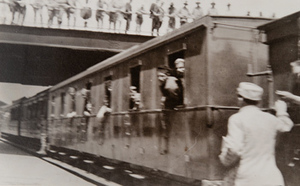 Soldiers leaning out of windows of a train in a station with a bridge overhead
