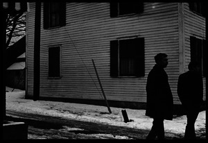 Two men walking past a house in the snow