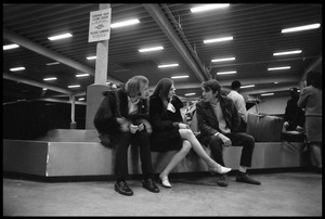 Stephen Stills (in heavy fur coat) and Judy Collins seated on an airport baggage carousel with an unidentified man