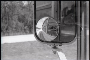 Side mirror on bus, with image of camera man reflected