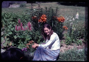 Anna seated with a dog in front of lupines, lilies, and other flowers; Montague Farm Commune