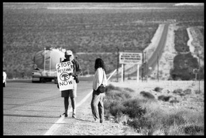 Activists on the road near the entrance to the Nevada Test Site, holding a sign reading 'Stop testing now': Nevada Test Site peace encampment