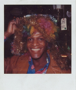 A Photograph of Marsha P. Johnson with a Rainbow Wig and Tinsel on Her Head