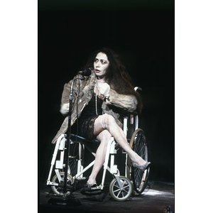 Woman in a wheelchair and theatrical makeup on stage during a Café Teatro performance.
